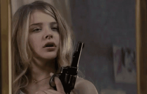 a young woman is holding a gun in front of a mirror and looking at herself .