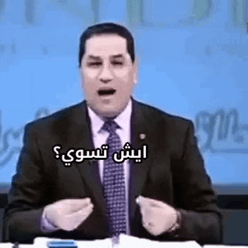 a man in a suit and tie is sitting at a table with his mouth open and talking in arabic .