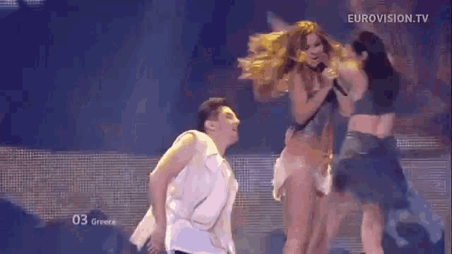 a woman is singing into a microphone while two dancers are dancing around her .