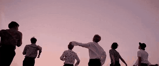 a group of people are standing next to each other in front of a pink sky at sunset .