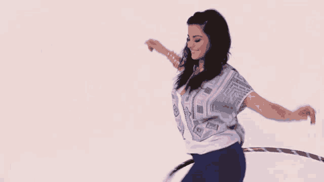 a woman in a white shirt and blue pants is playing with a pink hoop