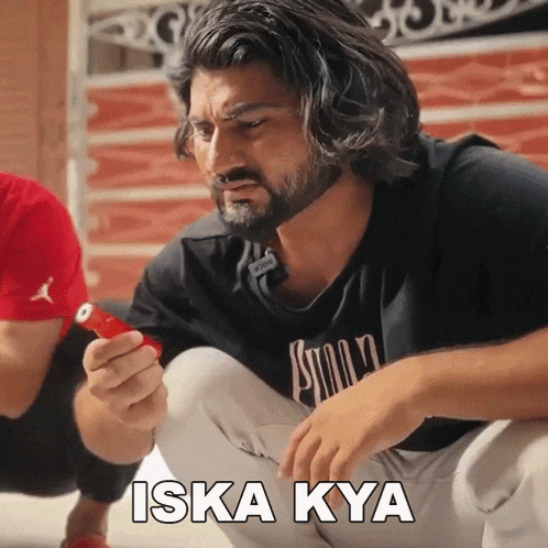 a man with a beard is squatting down and holding a red object with the words iska kya written on the bottom