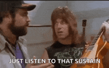 a man with a beard is holding a guitar and talking to another man who is holding a guitar .