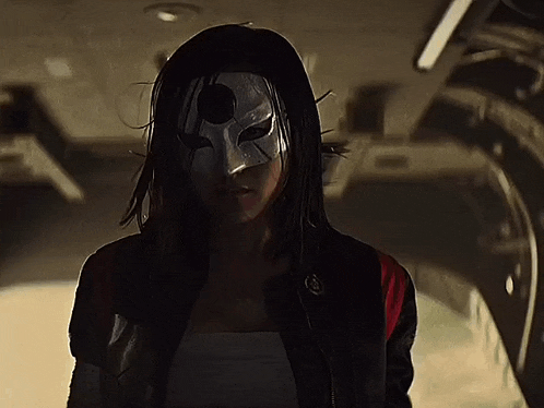 a woman wearing a mask and a black jacket is looking at the camera