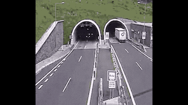 a truck is driving through a tunnel on a highway next to a mountain .