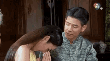 a man and a woman are sitting next to each other and the woman is covering her face with her hands .
