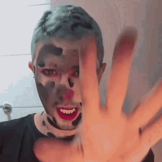 a man with makeup on his face is making a stop gesture with his hand