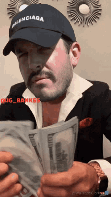 a man wearing a balenciaga hat is holding a large stack of money