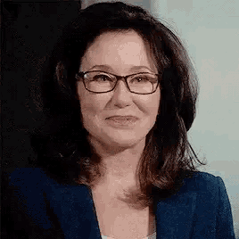 a woman wearing glasses and a blue suit is smiling .