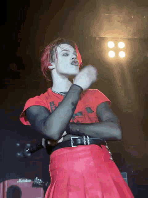 a man wearing a red skirt and a red shirt is dancing on stage