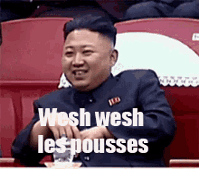 a man in a suit is sitting in a stadium with the words wesh wesh les pousses on the screen .