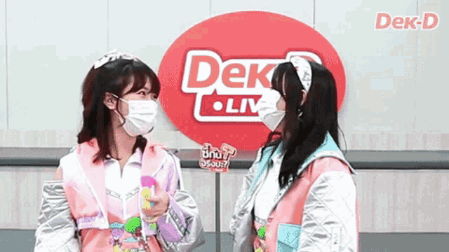 two girls wearing masks are standing in front of a sign that says dek live