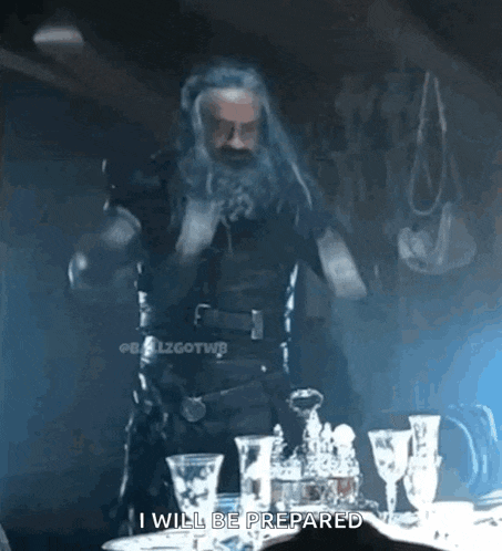 a man with a beard is standing in front of a table with wine glasses and says i will be prepared