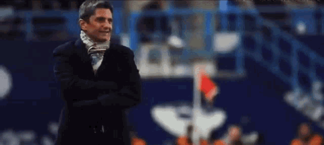 a man in a suit and scarf is standing on a soccer field