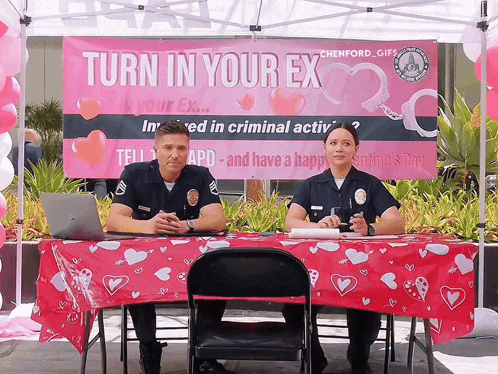 two police officers sit at a table under a sign that says " turn in your ex "