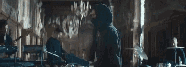 a man in a hooded jacket is playing a guitar in a band in a large room .