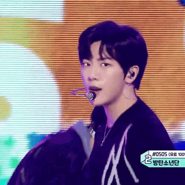 a young man is singing into a microphone while wearing a sweater with the letter a on it .