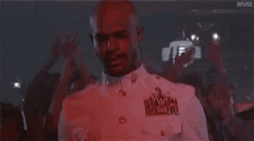 a man in a white shirt is dancing in front of a crowd in a red light .