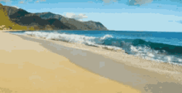a beach with mountains in the background and waves coming in