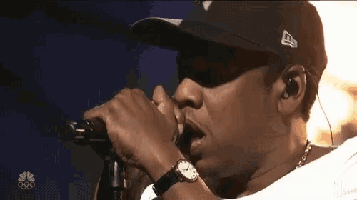 a man wearing a hat is singing into a microphone with a nbc logo in the background