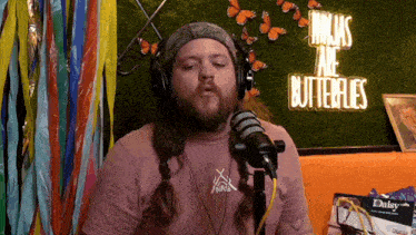 a man wearing headphones speaking into a microphone in front of a neon sign that says " ninjas are butterflies "