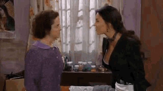 two women are standing next to each other in a room and talking .