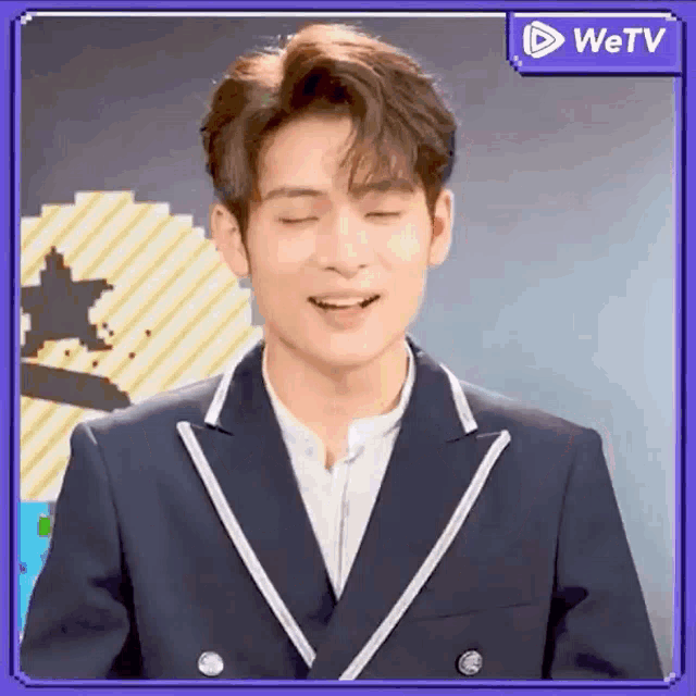 a man in a suit is smiling with his eyes closed and a wetv logo in the background .