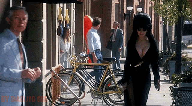 a woman in a black dress is walking down a sidewalk in front of a store