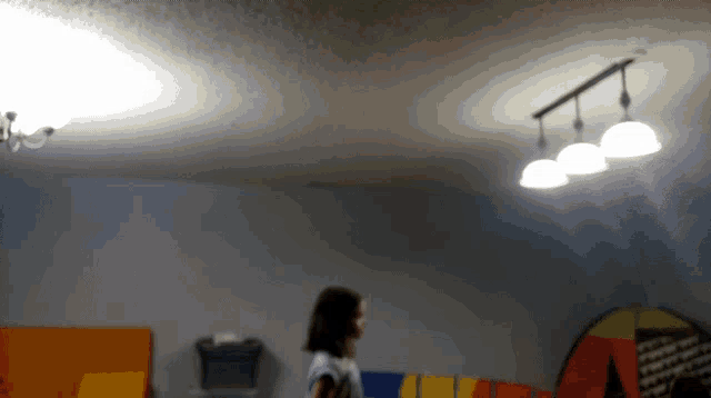 a blurry picture of a girl standing in a room with a colorful tent in the background