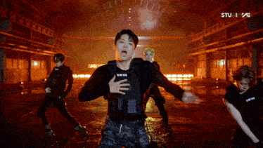a group of young men are dancing in a dark room and one of them is wearing a vest that says tw10