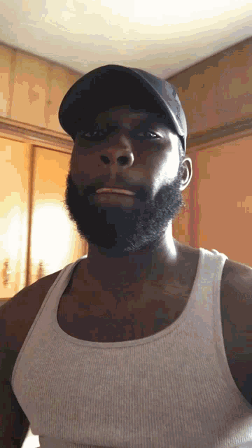 a man with a beard wearing a black hat and a tank top
