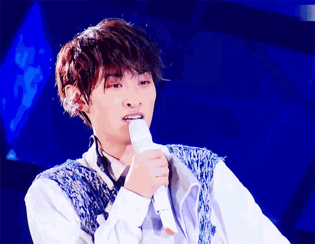 a young man is singing into a microphone with his mouth open