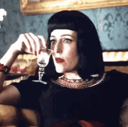 a woman in a black dress is drinking a glass of wine