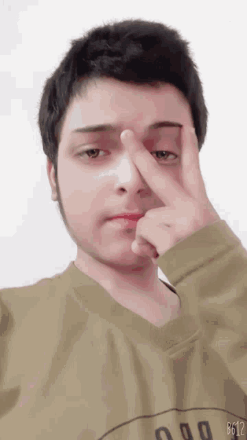 a young man wearing a green shirt with the number 000 on it holds his finger to his nose