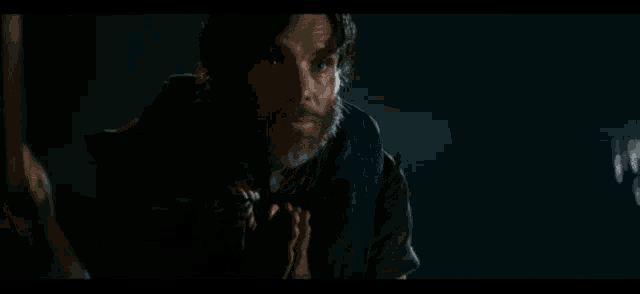 a man with a beard is standing in a dark room holding a sword .