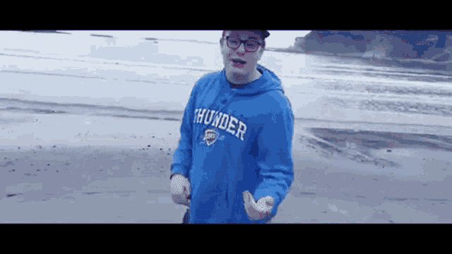 a young man wearing a blue thunder sweatshirt is standing on a beach