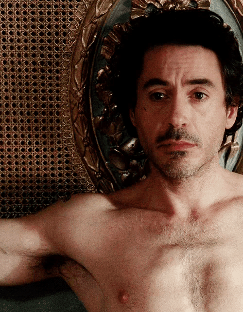 a shirtless man with a beard is laying on a wicker chair