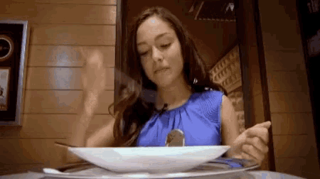 a woman in a blue top is sitting at a table with a plate of food