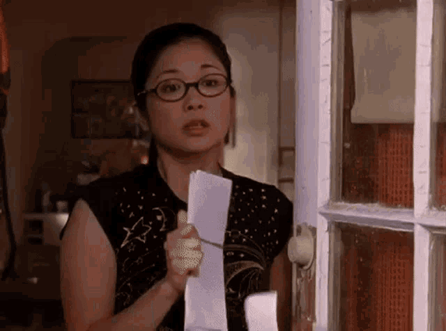 a woman wearing glasses is holding a piece of paper in her hand while standing in front of a door .