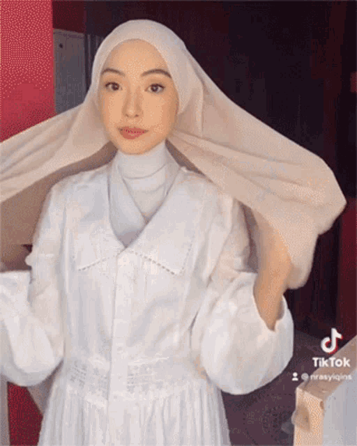 a woman wearing a white dress and a white hijab has tiktok written on the bottom