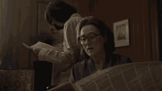 a woman reading a newspaper while another woman looks on