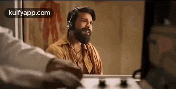 a man with a beard is wearing headphones while sitting in front of a computer .