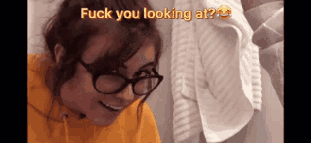 a woman wearing glasses and a yellow hoodie is smiling and says fuck you looking at .