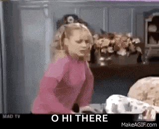 a woman in a pink shirt is standing in front of a table with the words o hi there on the screen .