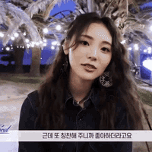 a woman wearing a denim shirt and earrings is sitting under a palm tree at night .