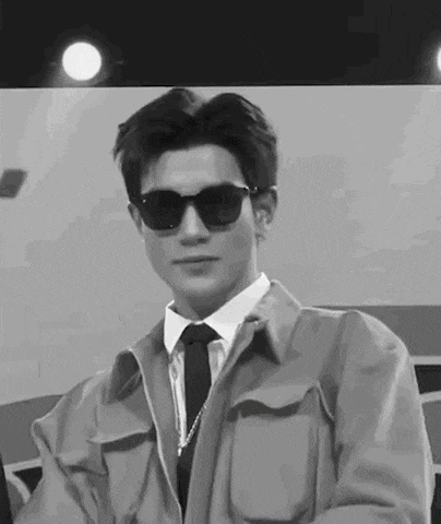a black and white photo of a man wearing sunglasses , a jacket and tie .