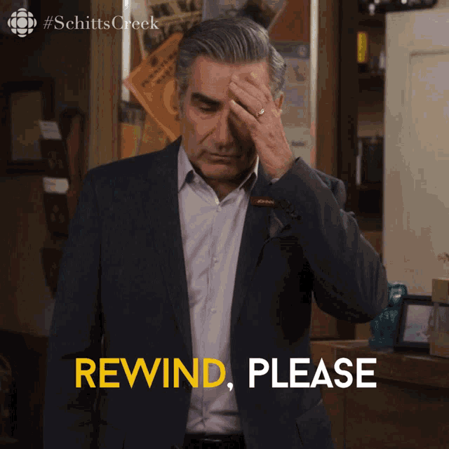 a man in a suit is holding his hand to his forehead and says rewind please