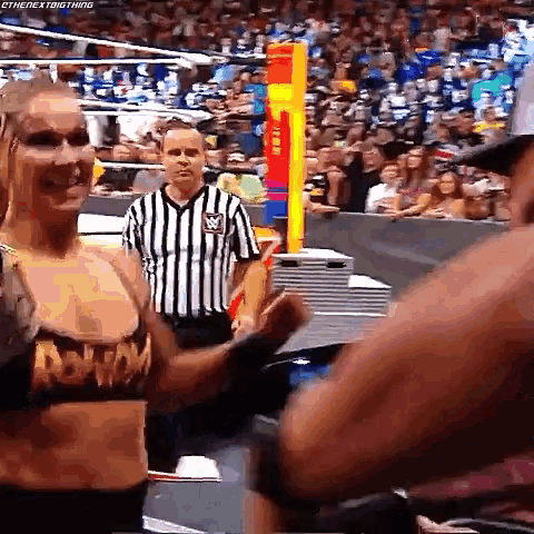 a female wrestler is standing next to a referee in a ring .
