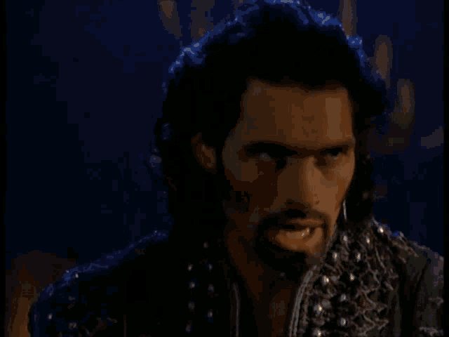 a man with a beard and long hair is standing in a dark room with candles in the background .