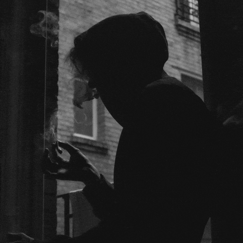 a man in a hoodie smoking a cigarette in front of a building